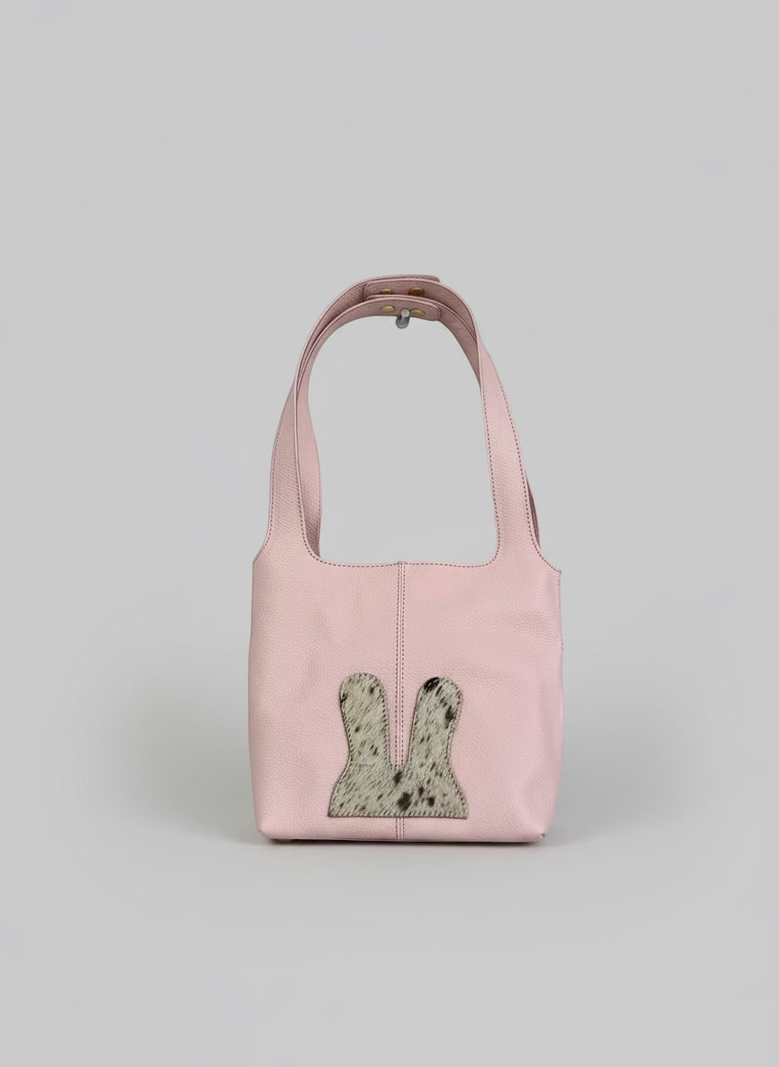 Pink handbag with a textured patch hanging on a white wall.