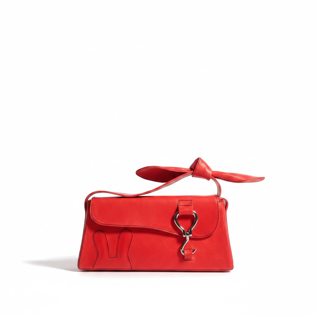 Design Girls World red vegetable-tanned leather mini shoulder bag with a knotted bow strap and bunny logo detail.